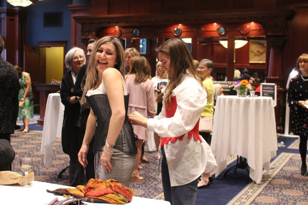 An event attendee laughing while getting fitted in a corset