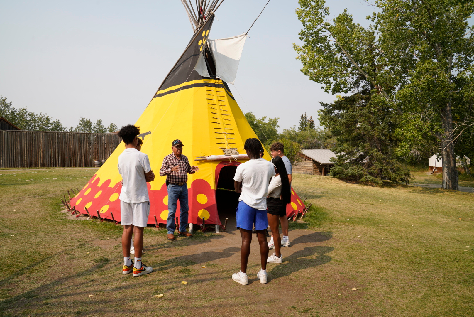An Indigenous man having a discussion with a group of young adults in front of the Yellow Otter Tipi