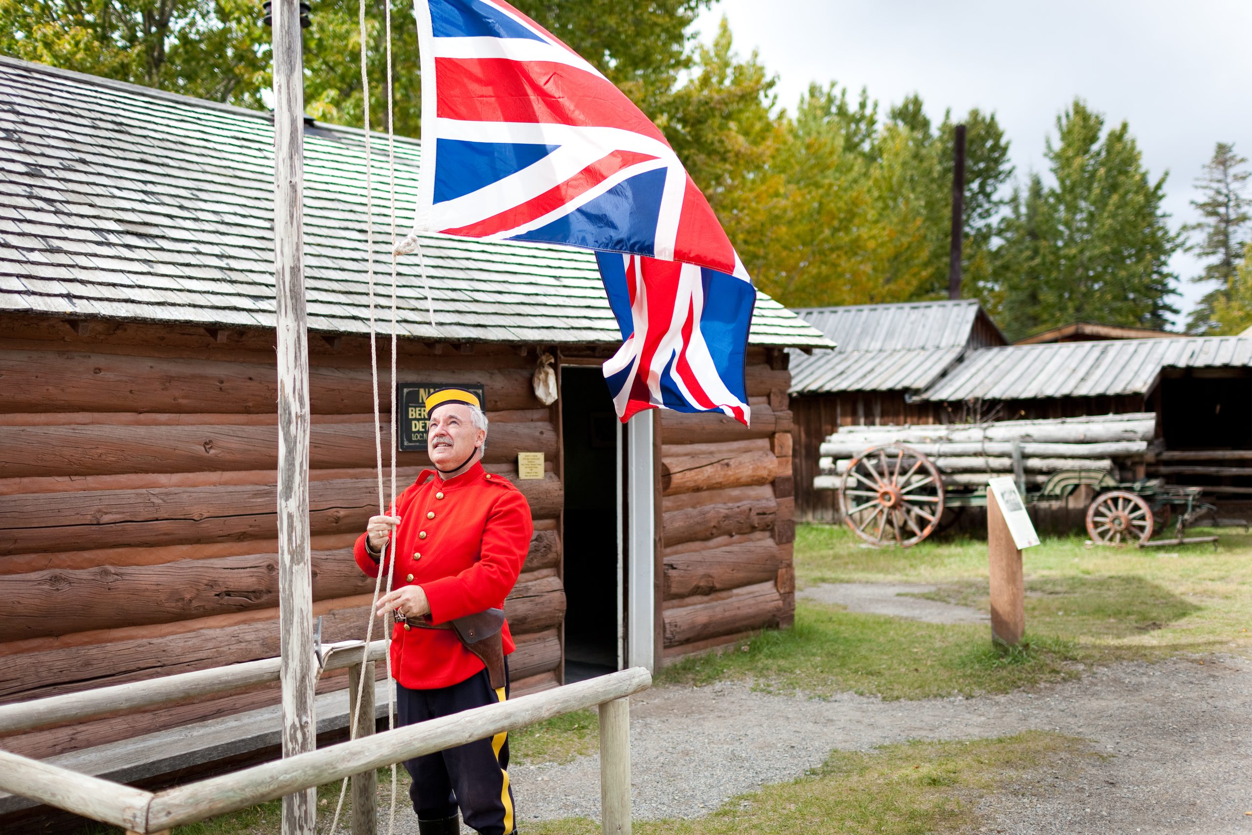 North West Mounted Police officer raising a British flag outside of the Berry Creek Barracks