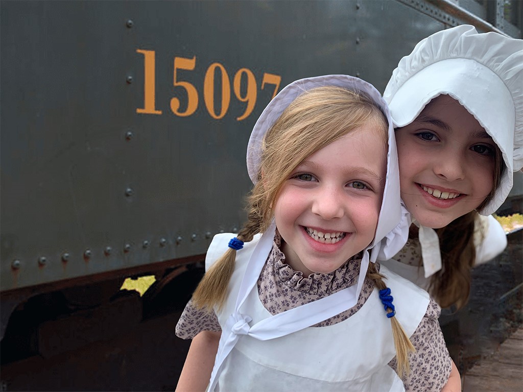 Two girls pose for a picture beside Heritage Park's steam train during an educational program.