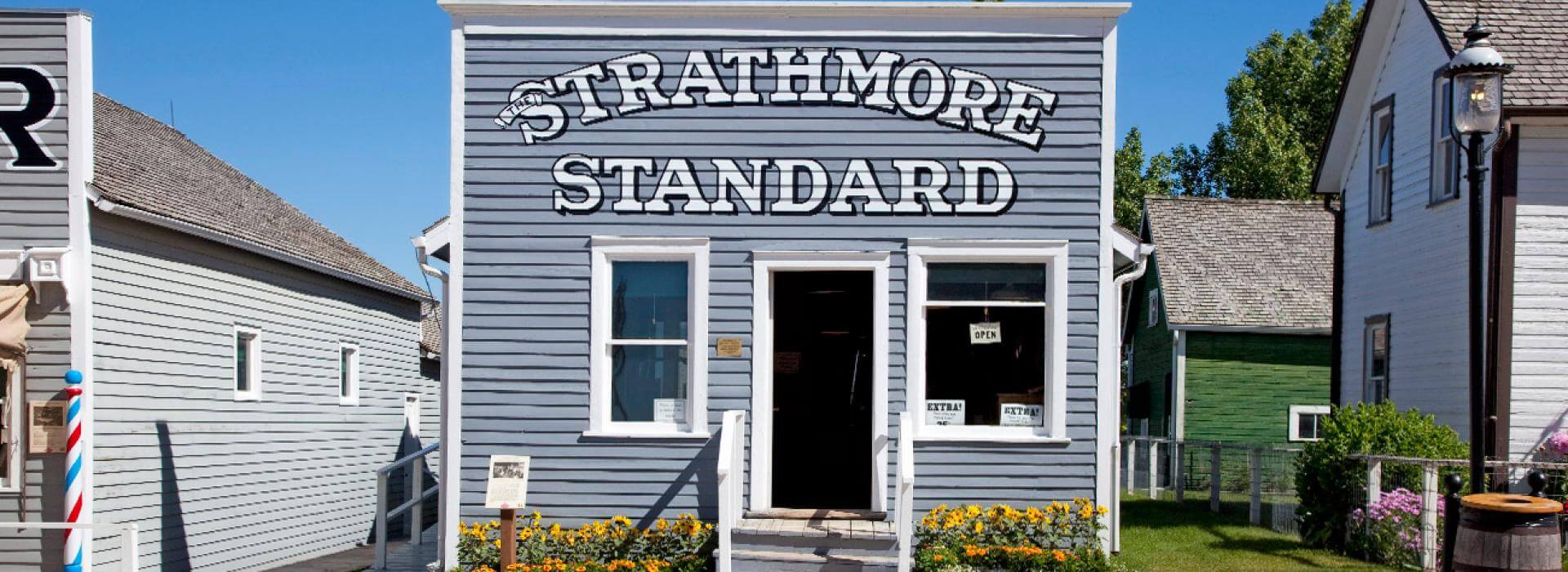 Grey 2 story building with a sign reading Strathmore Standard