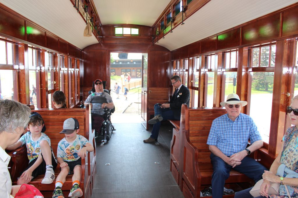 A turn of the century styled accessible railcar with a variety of people sitting in it, including a man in a wheelchair