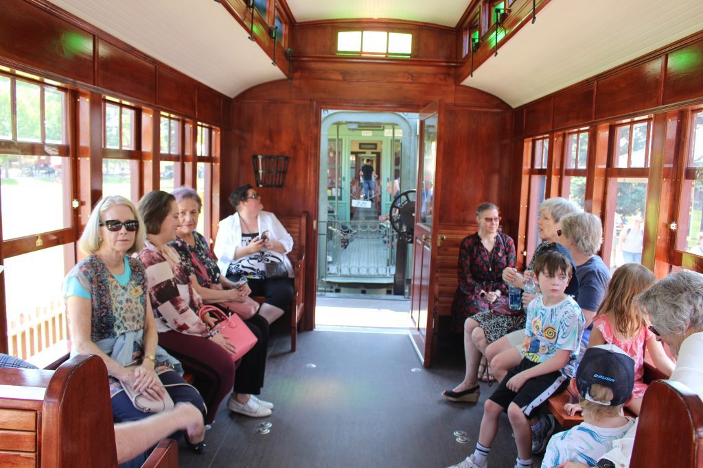 A turn of the century styled accessible railcar with a variety of people sitting in it.