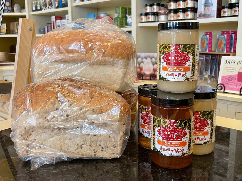 six jars of heritage park honey stacked next to some loaves of bread